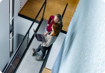 Two women standing in the ESYON office hallway looking at a laptop.