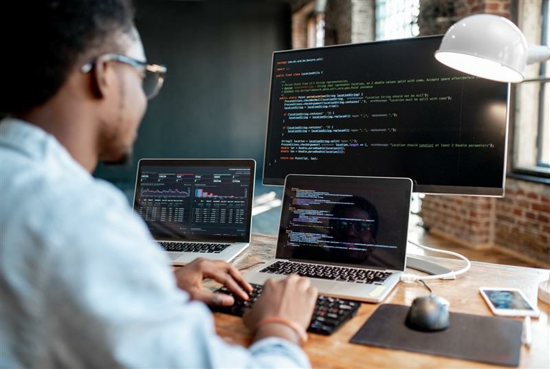 Person arbeitet an einem Computer und zwei Laptops