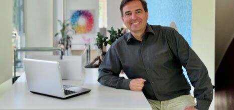 Ronny Büchner sits at a table in front of a laptop