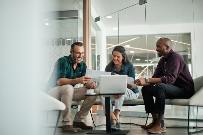 Three people sitting in front of a small laptop and looking at a piece of paper