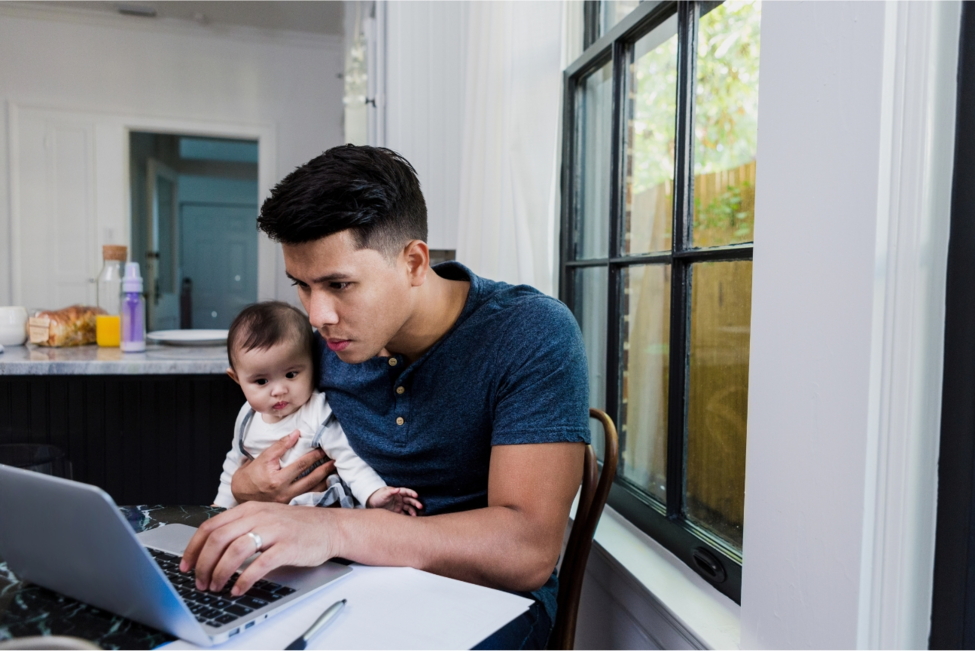 Mann arbeitet am Laptop mit Baby auf dem Schoss