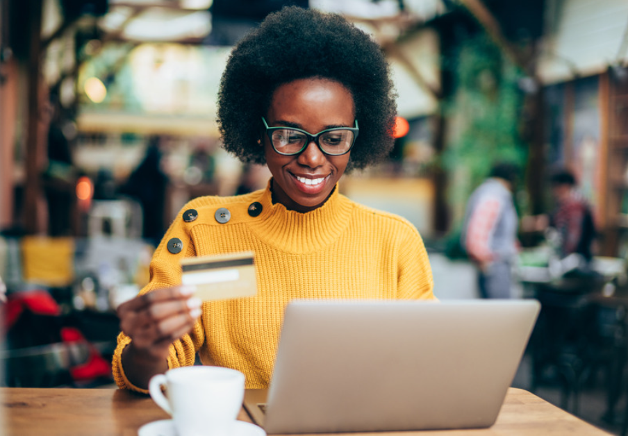 Woman in a yellow sweater using a laptop and holding a credit card