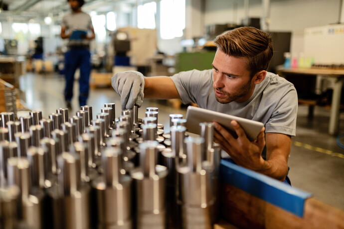 Mitarbeiter prüft Metallbauteile in der Produktion mit Tablet
