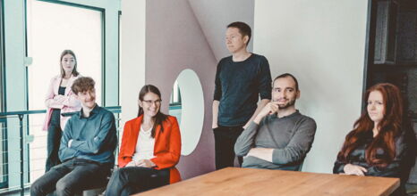 Six employees are having a meeting at a table and are smiling friendly