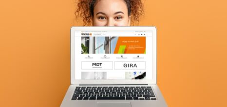 Frau hinter Laptop mit geöffneter Website auf orangefarbenem Hintergrund