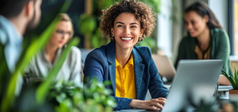 Smiling woman in yellow blouse working on laptop in green office setting