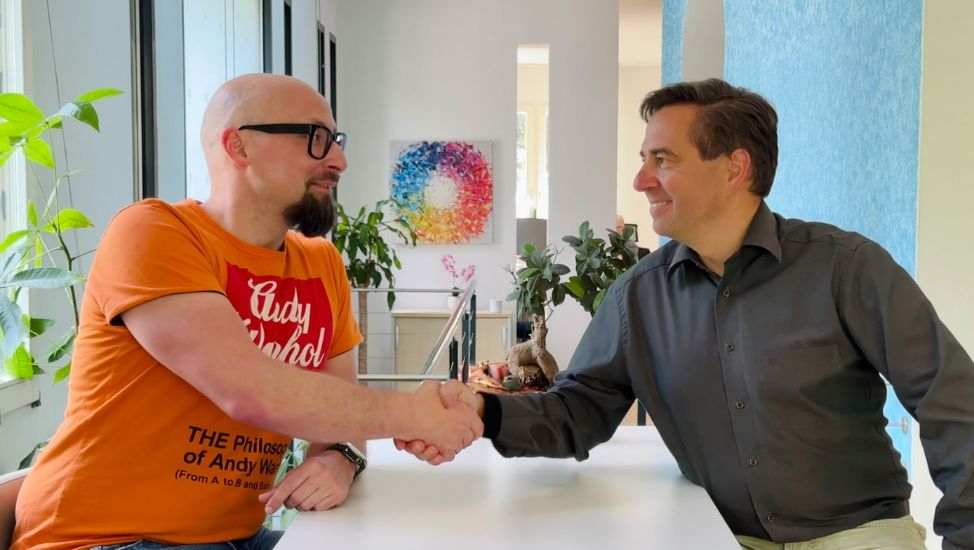 Ronny Büchner and Tino Favetto sit opposite each other and shake hands.