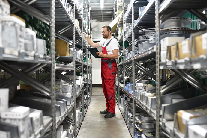 Mitarbeiter im roten Overall prüft Regale im Lager mit Autoersatzteilen