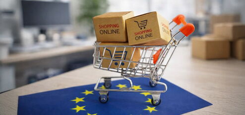 Online-Shopping-Warenkorb mit Paketen auf EU-Flagge vor unscharfem Bürohintergrund als Symbol für neue E-Commerce-Vorgaben