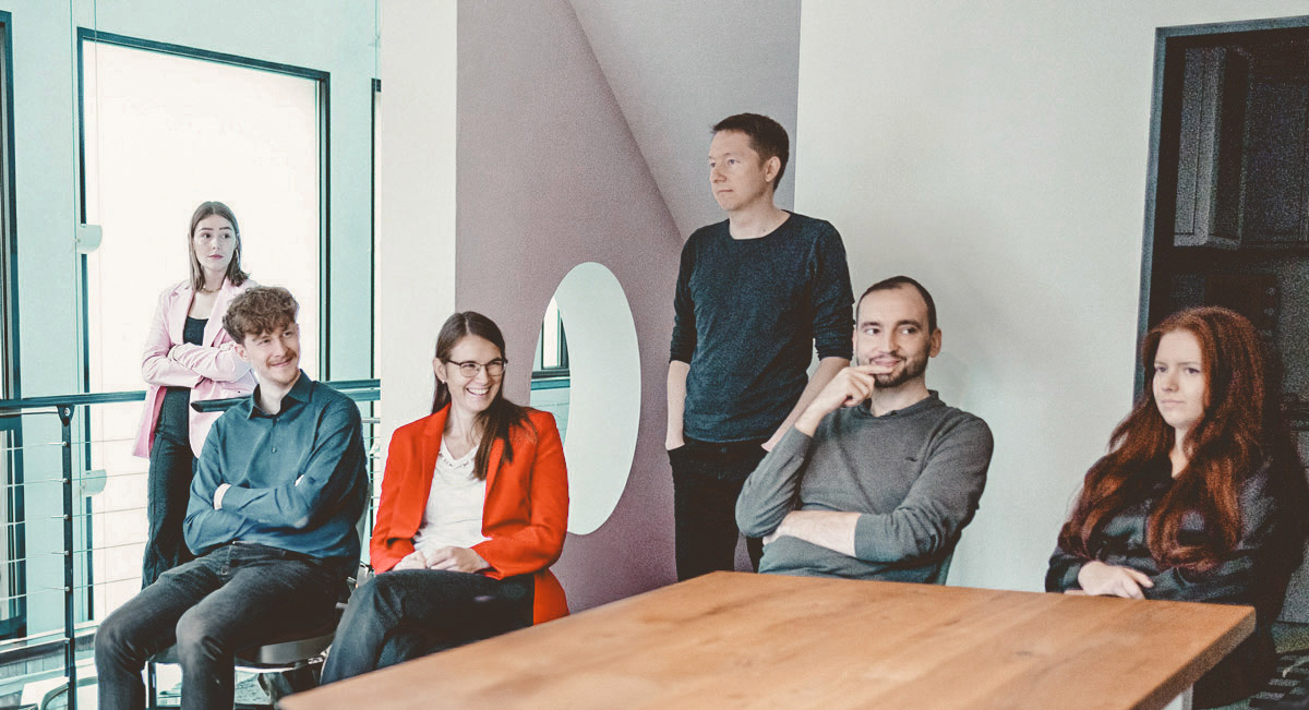 Six employees are having a meeting at a table and are smiling friendly